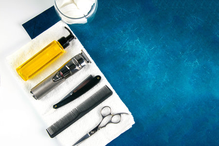 Scissors, haircut machine, gel, dangerous razor and comb stand on a white towel which stands on a...