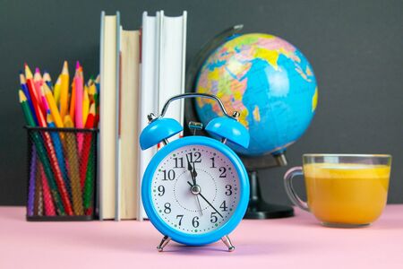 Coffe is in the foreground and behind him are a stack of books, a globe, a clock and a glass of pencils.の写真素材