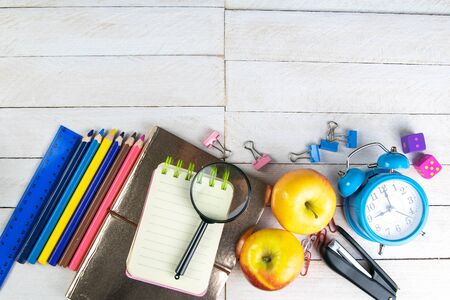 Various office stationery, notepad, clock, pencils, ooh, glasses, pen and two fresh apples on a white wooden table. Top view with copy space. Concept of office, education, workplace, school.の写真素材