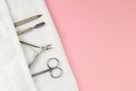 A set of cosmetic tools for manicure and pedicure. Manicure scissors, cuticles, saws on white towel stand on a pink background. Top views with clear space.の写真素材