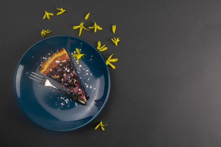 Slices of blueberry mousse cake with mirror glaze decorated berries and leaves of mint on a blue plate are on black table, close up. Top views.の写真素材