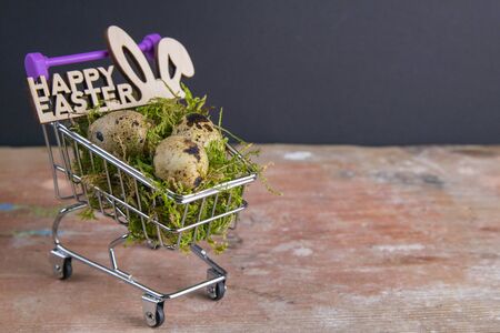 Quail eggs stand in a basket of supermarket filled with moss next is a sign of the Happy Easter stand on a wooden table. Top views with clear space.の写真素材