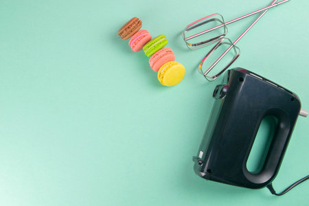 Colorful macaroons and mixer on mint background. Top views with clear space.