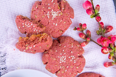 Beetroot oatmeal cookie stands on a white towel, next to a flowering branch with rose flowers. Top...