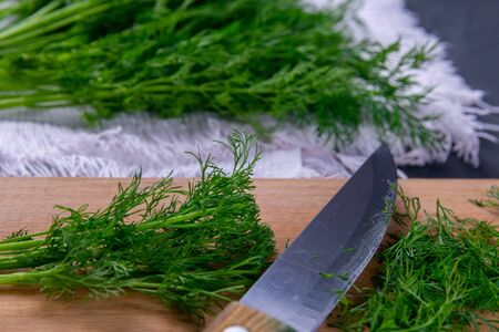 Fresh cut green dill and metal knife on wooden chopping board on white towel and black grunge kitchen table background. Cutting greens for adding to soup or salad. Healthy food.の写真素材