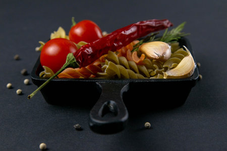 Italian food raw pasta fusilli with tomatoes, rosemary, hot pepper and garlic in a small frying pan....