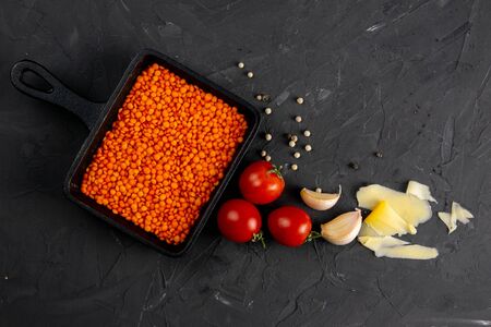Still life food set on dark background. Concept shealthy eating. Lentils in frying pan, cheese, garlic and cherry tomato. Top views, close-up.の写真素材