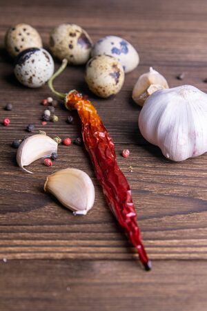 Spicy, garlic, hot red peppers, quail eggs on a dark wooden background. Close-upの写真素材