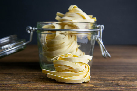 Pasta fettuccine In a glass jar on a wooden table. Front views, close-up.