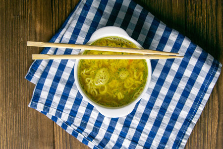 A noodles on white dish with chopsticks wood on an blue and white towel stand on a wooden table. Top...