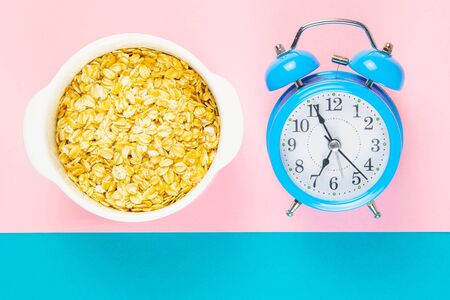Blue alarm clock with oatmeal on a pink and blue background. Healthy nutrition concept. Top views with clear space.の写真素材