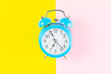 Ringing twin bell classic alarm clock isolated on yellow and pink pastel colorful geometric...