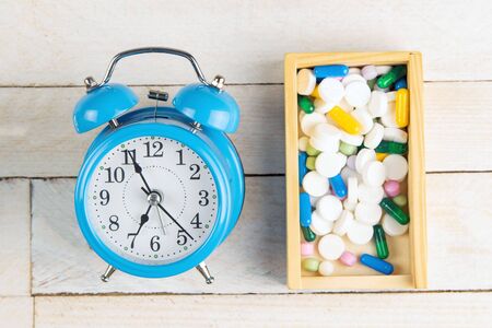 Time to accept tablets. Tablets in a wooden box along with a blue watch on a white wooden table.の写真素材