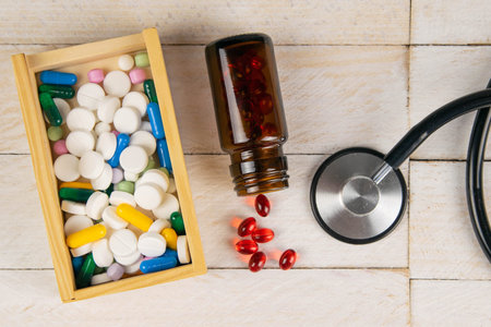 Pills in botle and wooden box with stethoscope and heart on white wooden table. Medical concept. Top...