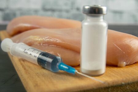 Injection syringe in raw chicken pieces, concept of injection of GMOs into the meat. Close-up.の写真素材