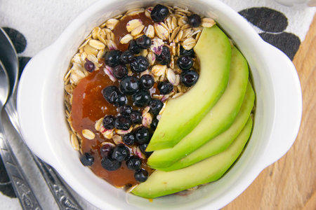 Healthy breakfast with oatmeal with bluberrys, avocado and apricot jam on wooden board. Top views...
