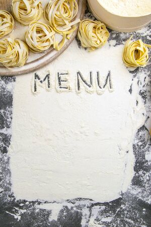 Homemade uncooked pasta tagliatelle on black background. Making fresh italian tagliatelle . The word 'menu' from flour. Banner.の写真素材