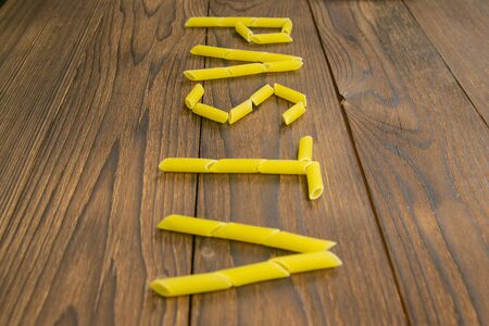 The word pasta is made from pasta Pene Lisce on a wooden table. Front views.の写真素材