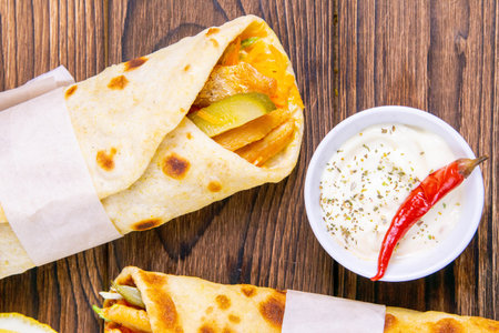 Two doner kebab with souce, vegetables and fries in pita bread close-up on a wooden table.