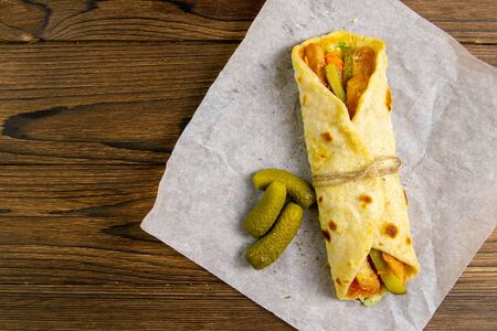 Delicious Turkish doner kebab on pita bread with shaved roasted meat off a traditional vertical rotisserie served with fresh salad ingredients on rustic paper, stand on wooden table.の写真素材