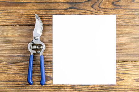 Blue pruning shears with a white sheet of paper on wood background. Top views with clear space.の写真素材