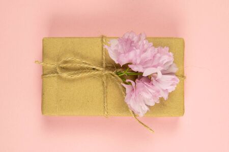 Gift boxes wrapped of craft paper and burlap ribbon with pink flowers on the pink background, top view, close-up.の写真素材