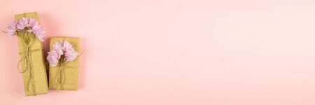 Two gift boxes wrapped of craft paper and burlap ribbon with pink flowers on the pink background, top view with clear space.の写真素材