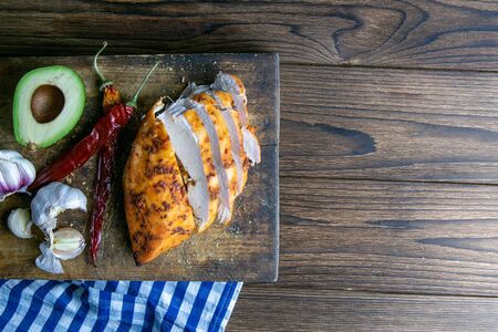 Spicy baked chicken breast with peper, rosemary, avocado and garlic on wooden cutting board on wooden table. Top views with clear space.の写真素材