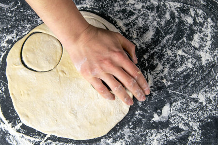 The process of cutting circle from the dough on a dark background. Top views, close-up.