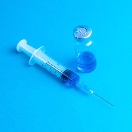 Glass vials and a medical syringe with a coronavirus vaccine on a blue background.