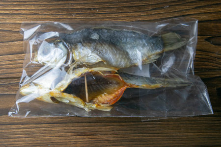 Dried salted crucian fishes in a transparent package on wooden background. Snack to beer.