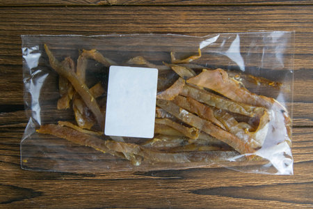 Dried carp fish sticks in a transparent package with a white label appetizer to beer on wooden...
