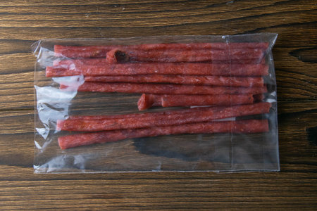Dry salmon sticks in a transparent package isolated on wooden background. Snack Fish to beer. Close...