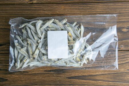 Dried salted anchovies in a transparent package with a white label on wooden background. Snack Fish to beer. Close up.の写真素材