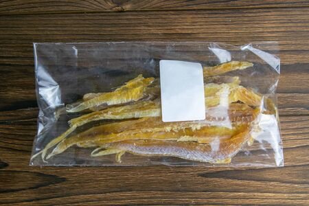 Dried tuna fillet in a transparent package with white label appetizer to beer on wooden background. Snack Fish to beer. Close up.の写真素材
