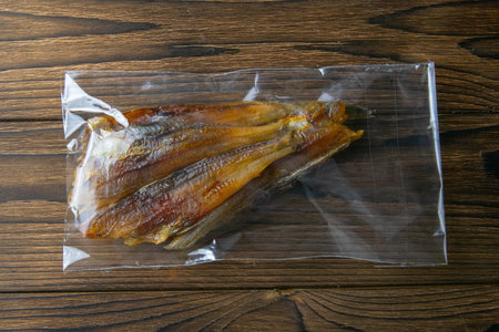 Dried blue whiting fish in a transparent package appetizer to beer on wooden background. Snack Fish...