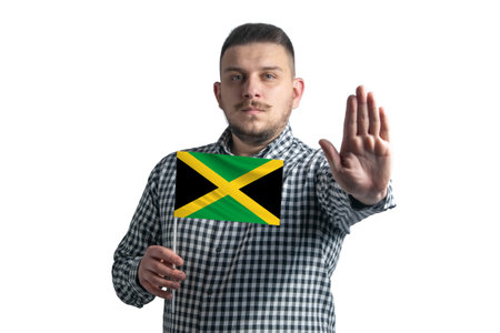 White guy holding a flag of Jamaica and with a serious face shows a hand stop sign isolated on a white background.の写真素材
