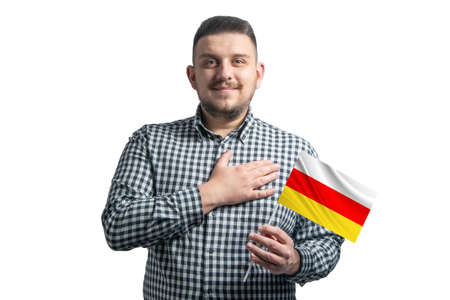 White guy holding a flag of South Ossetia and holds his hand on his heart isolated on a white background With love to South Ossetia.の写真素材