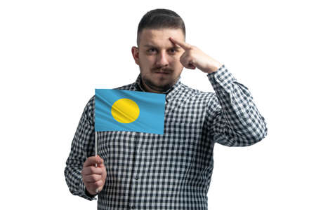 White guy holding a flag of Palau and a finger touches the temple on the head isolated on a white backgroundの写真素材