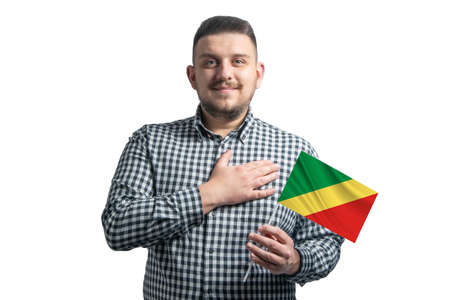 White guy holding a flag of Republic of the Congo and holds his hand on his heart isolated on a white background.の写真素材