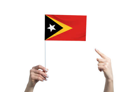 A beautiful female hand holds a East Timor flag to which she shows the finger of her other hand, isolated on white background.の写真素材