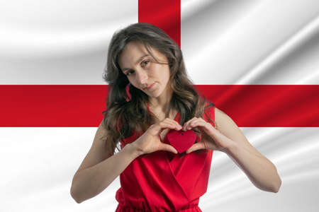 Love England. A girl holds a heart on her chest in her hands against the background of the flag of England. The concept of patriotism.の写真素材