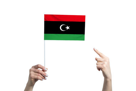 A beautiful female hand holds a Libya flag to which she shows the finger of her other hand, isolated on white background.の写真素材