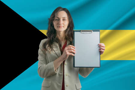 Study in Bahamas. Beautiful woman holding a sheet of paper in her hands. Girl on the background of the flag of Bahamas.の写真素材