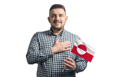 White guy holding a flag of Greenland and holds his hand on his heart isolated on a white background With love to Greenland.の写真素材