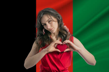 Love Afghanistan. A girl holds a heart on her chest in her hands against the background of the flag of Afghanistan. The concept of patriotism.の写真素材