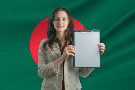 Study in Bangladesh. Beautiful woman holding a sheet of paper in her hands. Girl on the background of the flag of Bangladesh.の写真素材