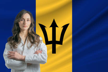 Medicine in Barbados. Happy beautiful female doctor in medical coat standing with crossed arms against the background of the flag of Barbados.の写真素材