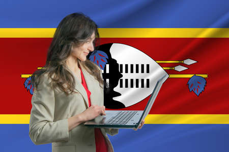 Freelance in Esvatini Beautiful young woman freelancer uses laptop computer against the background of the flag of Esvatini.の写真素材