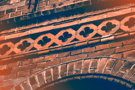 Old red brick house with ornaments. The walls have small cracks and chips. Patterns rounded.